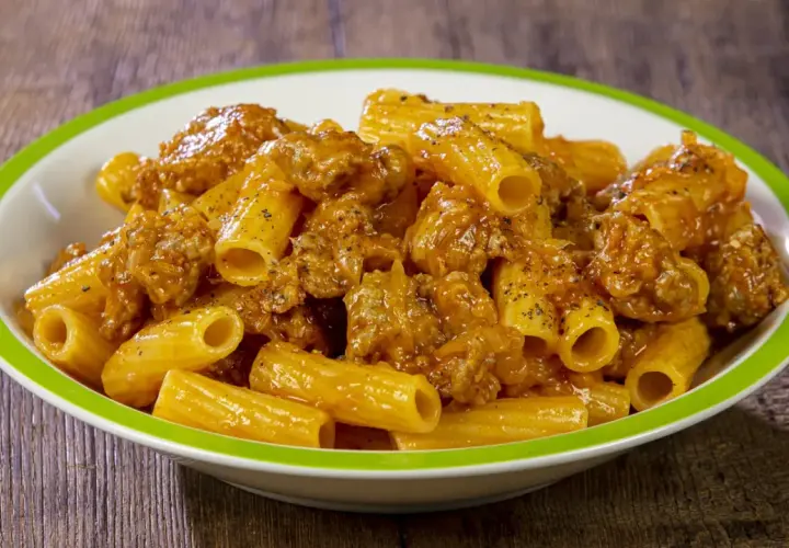 Piatto di rigatoni conditi con un ricco sugo di salsiccia, cosparso di pepe nero.