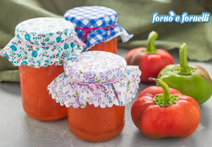 Barattoli di crema di peperoni fatti in casa, decorati con stoffe floreali e a quadretti, accanto a peperoni freschi.
