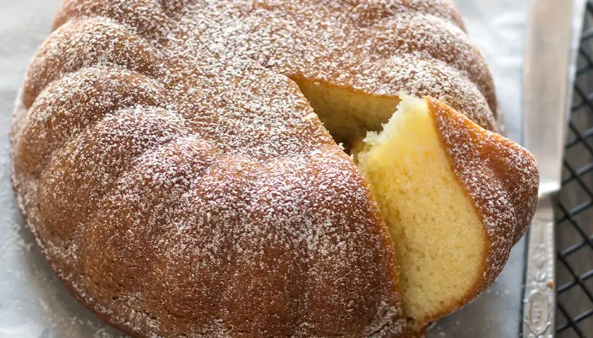 Una soffice torta allo yogurt, cosparsa di zucchero a velo, con una fetta tagliata che ne rivela l'interno dorato e invitante.