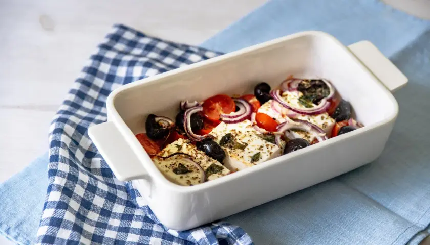 Feta al forno con pomodorini, olive nere e cipolla rossa, condita con erbe aromatiche.