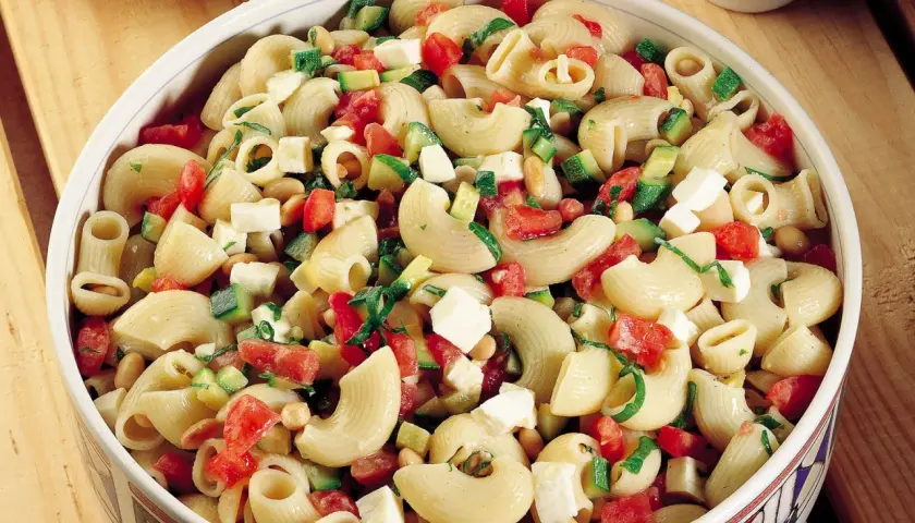 Un invitante piatto di pasta fredda con zucchine, pomodorini, cubetti di formaggio e fagioli, perfetto per un pasto estivo.