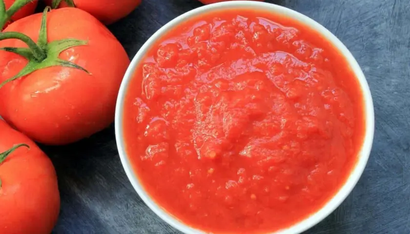 Una ciotola di passata di pomodoro, con pomodori freschi sullo sfondo.