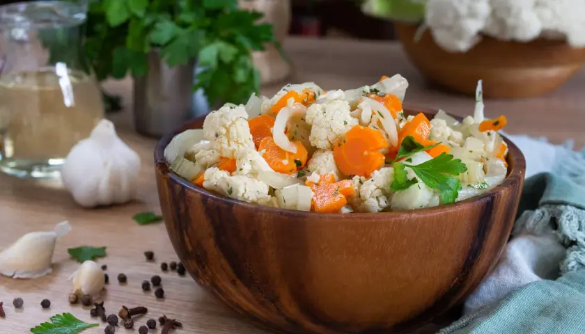 Una ciotola di legno piena di giardiniera fatta in casa, con cavolfiore, carote e cipolle, guarnita con prezzemolo fresco.