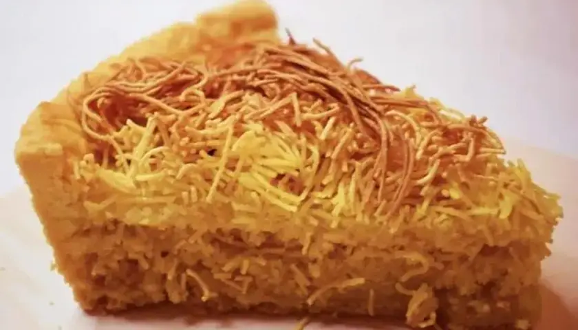 Una fetta di torta di tagliatelle, con la crosta dorata e un ripieno soffice, decorata con fili croccanti.