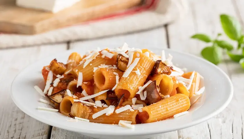 Piatto di pasta alla norma ricetta con melanzane fritte, pomodoro e ricotta salata grattugiata.