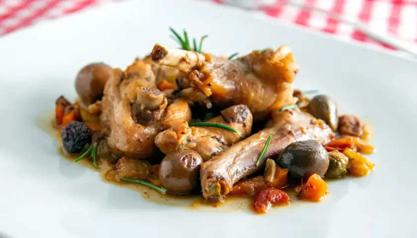 Coniglio alla cacciatora ricetta della nonna: succulenti pezzi di coniglio con olive, pomodorini e rosmarino, un classico sapore di casa.