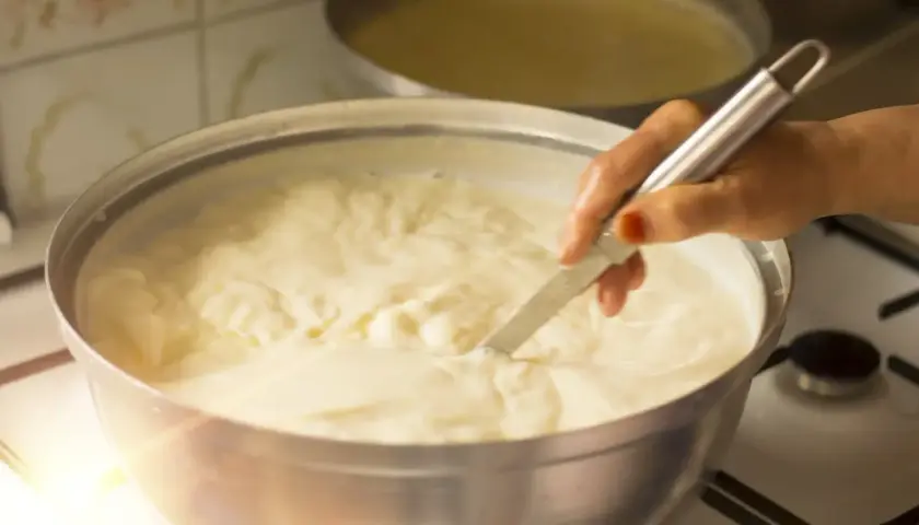 Mano che mescola un pentolone pieno di cremoso yogurt fatto in casa, pronto per essere gustato.