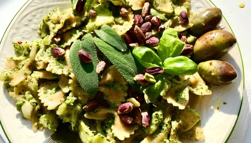 Farfalle condite con un cremoso pesto di salvia, guarnite con pistacchi, basilico e olive verdi.