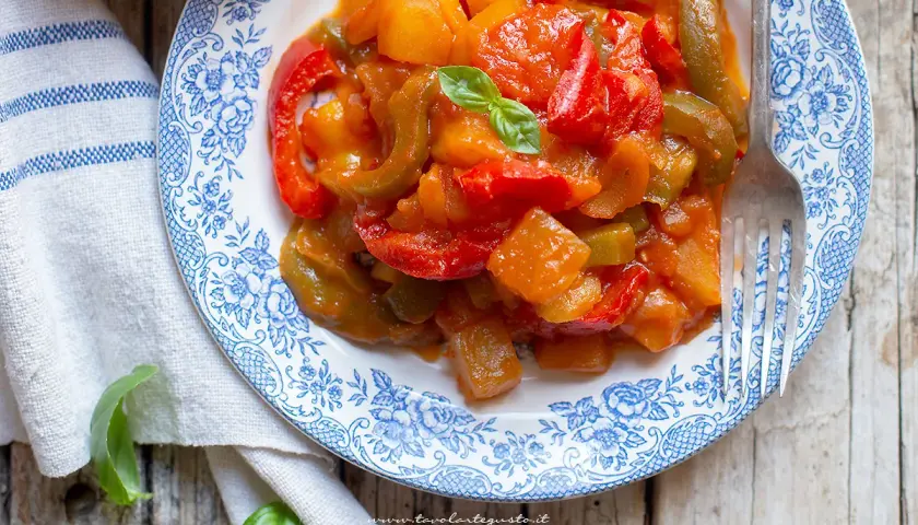 Un piatto di peperonata con patate, colorata e saporita, guarnita con basilico fresco.