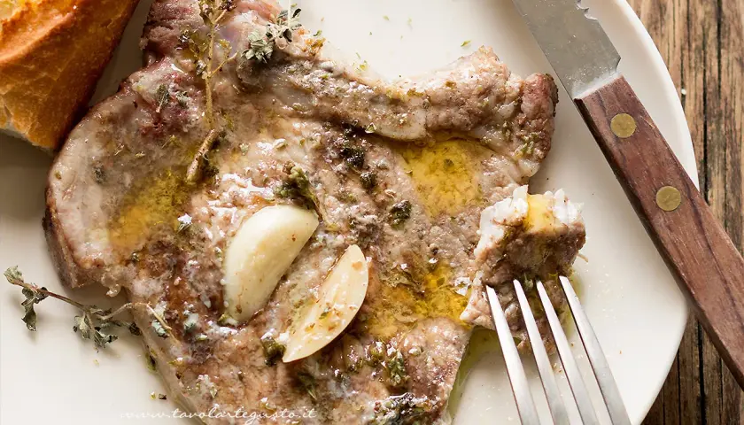 Succulente braciole di maiale cotte con aglio e erbe aromatiche, servite con pane croccante e un filo d'olio.