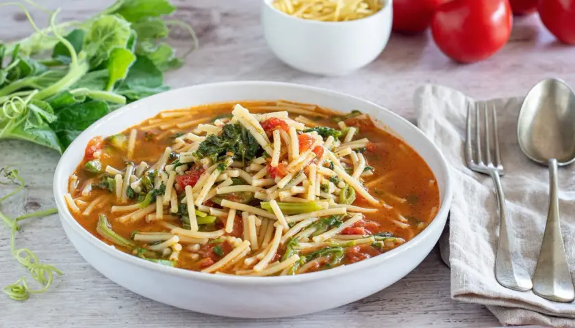 Un piatto fumante di pasta con i tenerumi, un classico siciliano, con pomodoro e verdure fresche.