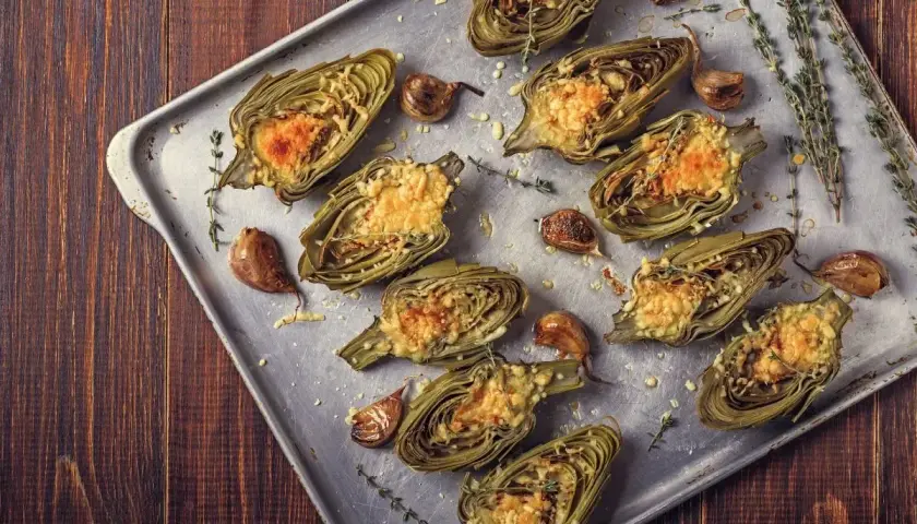 Carciofi al forno morbidi, ripieni e gratinati, con aglio e timo su teglia metallica.