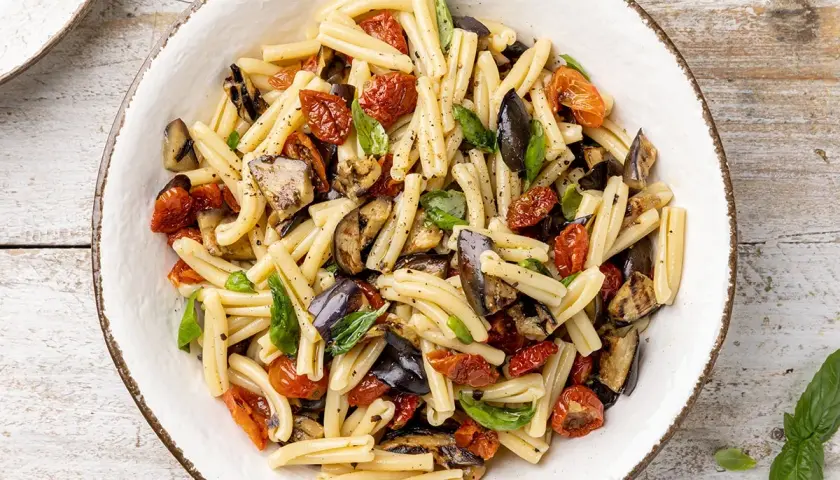 Pasta fredda con melanzane grigliate, pomodorini secchi e basilico fresco, un piatto estivo colorato e saporito.