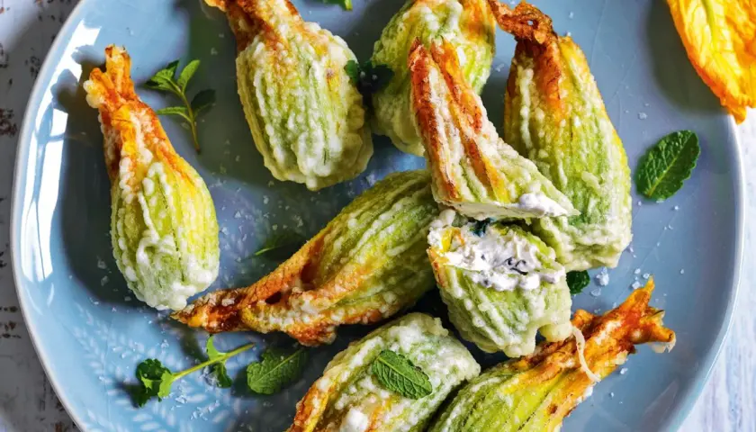 Fiori di zucca fritti, ripieni di formaggio cremoso e guarniti con menta fresca su un piatto blu.