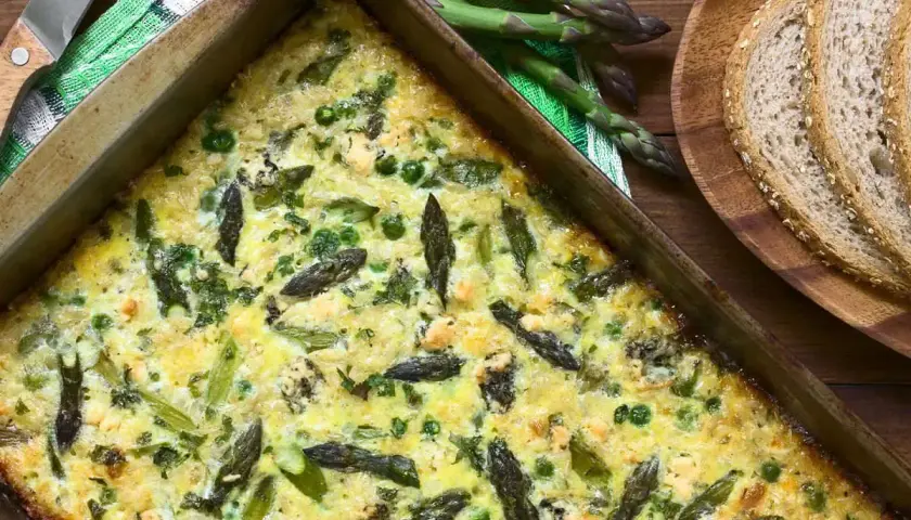 Frittata di asparagi appena sfornata, ricca di verdure e formaggio, pronta per essere gustata con pane integrale.