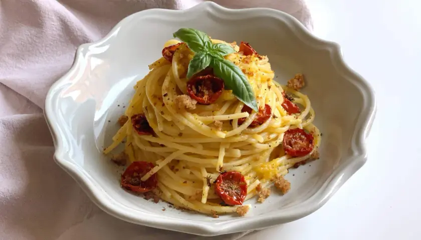 Un piatto di spaghetti conditi con pomodorini gialli secchi, basilico fresco e pangrattato croccante.