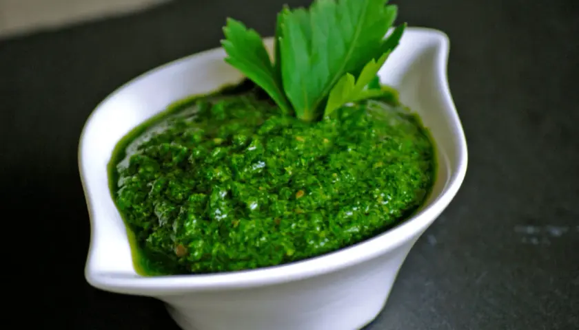 Una ciotola bianca contiene una vibrante ricetta salsa verde leggera, guarnita con prezzemolo fresco.