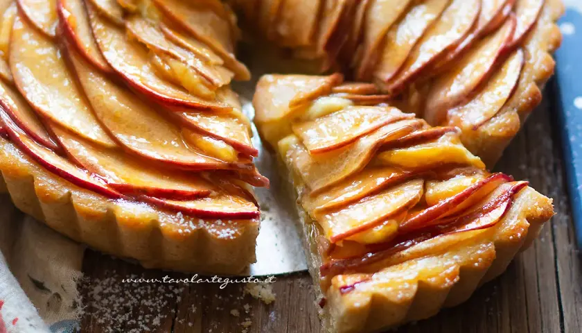 Una fetta di crostata di mele dorata, con mele caramellate disposte a rosa su una base friabile.