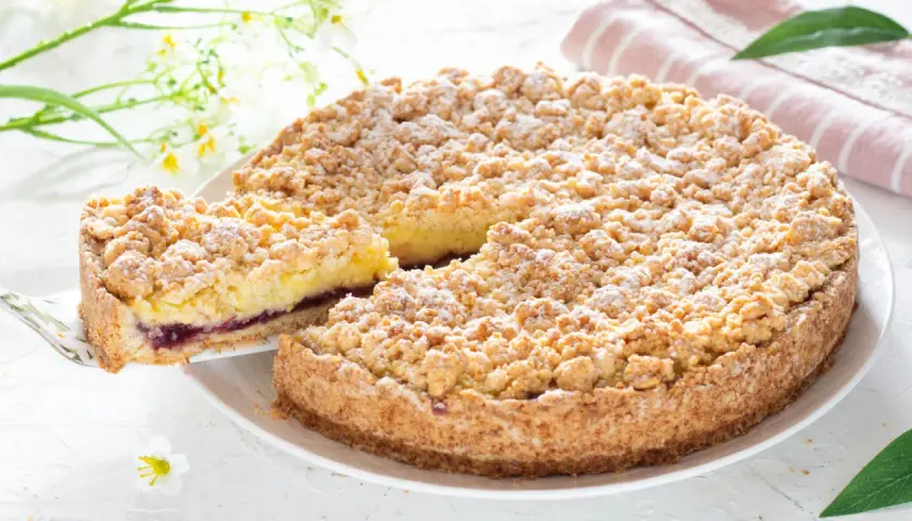 Sbriciolata alla crema con confettura di frutti di bosco, cosparsa di zucchero a velo. Una fetta è stata appena tolta, rivelando il ripieno.