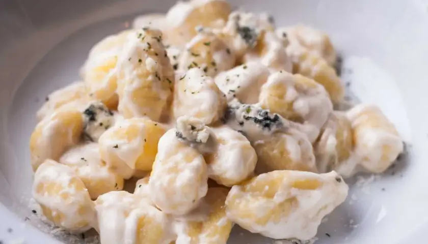 Gnocchi al gorgonzola cremosi, con pezzetti di formaggio blu e erbe aromatiche, serviti in un piatto bianco.