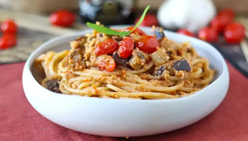 Un piatto invitante di pasta e melanzane alla napoletana, condito con pomodorini freschi e basilico.