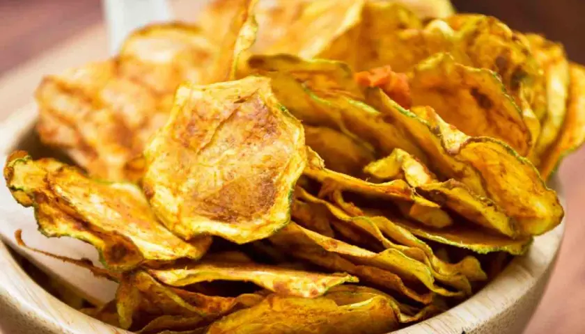 Croccanti chips di zucchine dorate, un'alternativa salutare e gustosa alle patatine, servite in una ciotola di legno.
