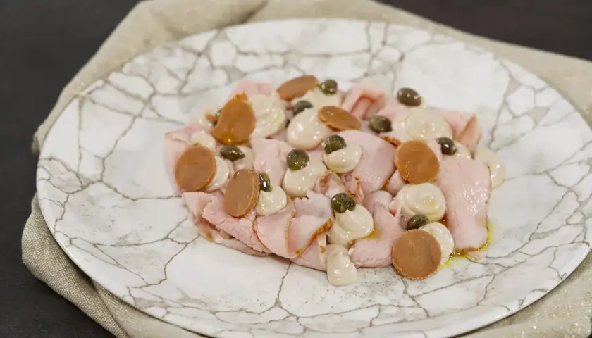 Vitello tonnato ricetta: fettine rosa di vitello, salsa tonnata, capperi e acciughe su piatto di marmo.