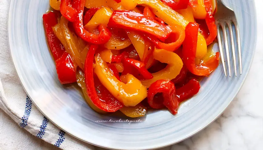 Piatto di peperoni in agrodolce, rossi e gialli, conditi con olio e spezie, pronti per essere gustati.