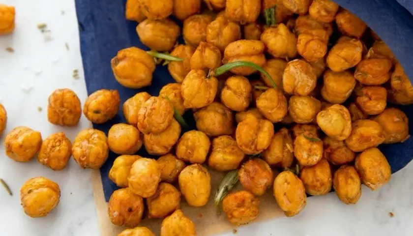 Ceci croccanti al forno, dorati e speziati, versati da un sacchetto blu. Perfetti per uno snack salutare.