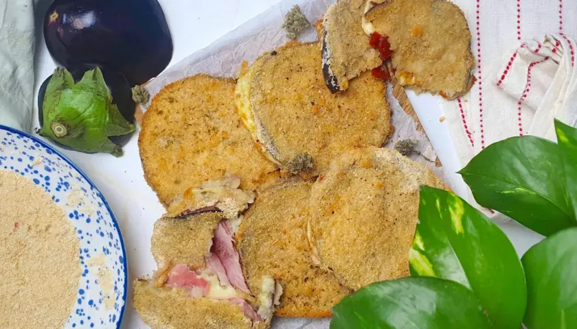 Cordon bleu di melanzane impanati e fritti, ripieni di prosciutto e formaggio filante. Accanto, melanzane fresche e pangrattato.
