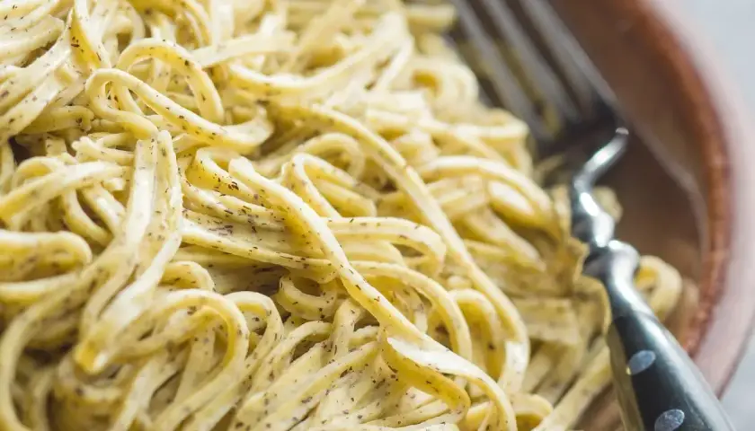 Un primo piatto invitante: tagliolini al limone, conditi con una crema delicata e erbe aromatiche, pronti per essere gustati con una forchetta.