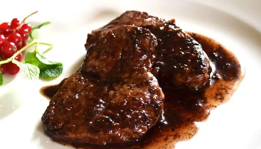 Tre fette di brasato di manzo succulento in salsa scura, guarnite con ribes rossi e menta fresca.