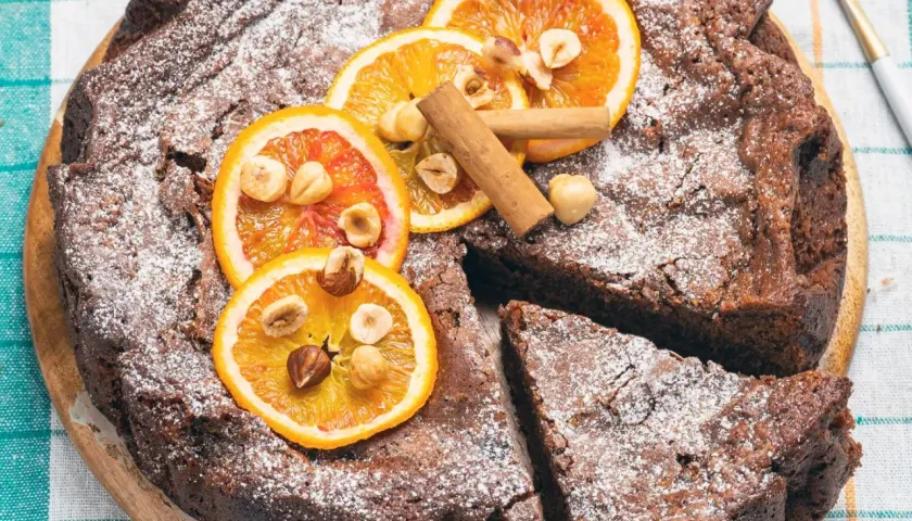 Deliziosa torta di pane al cioccolato, cosparsa di zucchero a velo, decorata con fette d'arancia, nocciole e cannella.