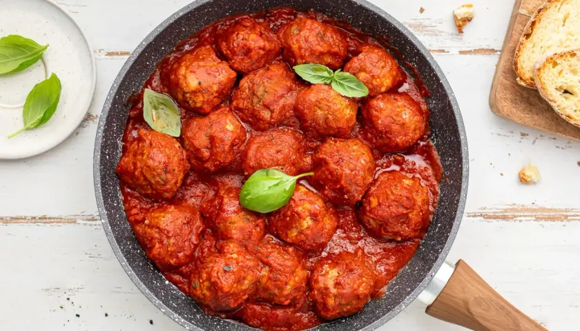 Succulente polpette di carne in padella, immerse in un ricco sugo di pomodoro, guarnite con foglie di basilico fresco.