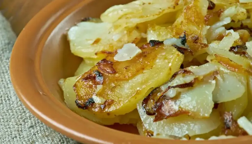 Patate alla lionese dorate e croccanti, servite in una ciotola di terracotta. Un classico saporito.