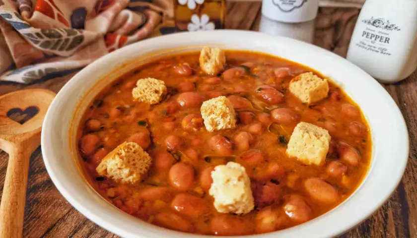 Una ciotola di zuppa di fagioli fumante, guarnita con crostini croccanti, pronta per essere gustata.