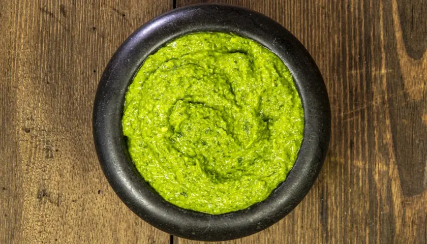 Un mortaio di pietra nera contiene un vibrante pesto alla genovese, pronto per condire la pasta.