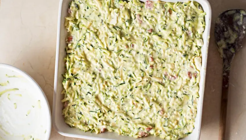 Sformato di zucchine pronto per essere infornato, con zucchine grattugiate e un cremoso impasto.