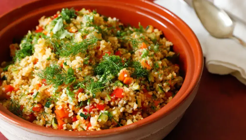 Tabulè di verdure fresco e colorato, con pomodori, zucchine e erbe aromatiche, servito in una ciotola di terracotta.