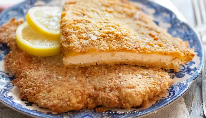 Due cotolette al forno dorate e croccanti, servite su un piatto blu con spicchi di limone.