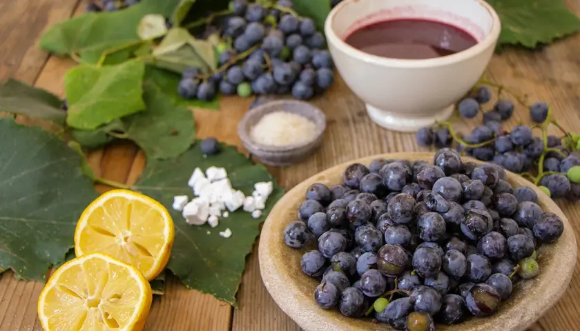 Uva fragola fresca, limone, zucchero e una ciotola di succo scuro, ingredienti per una deliziosa marmellata.