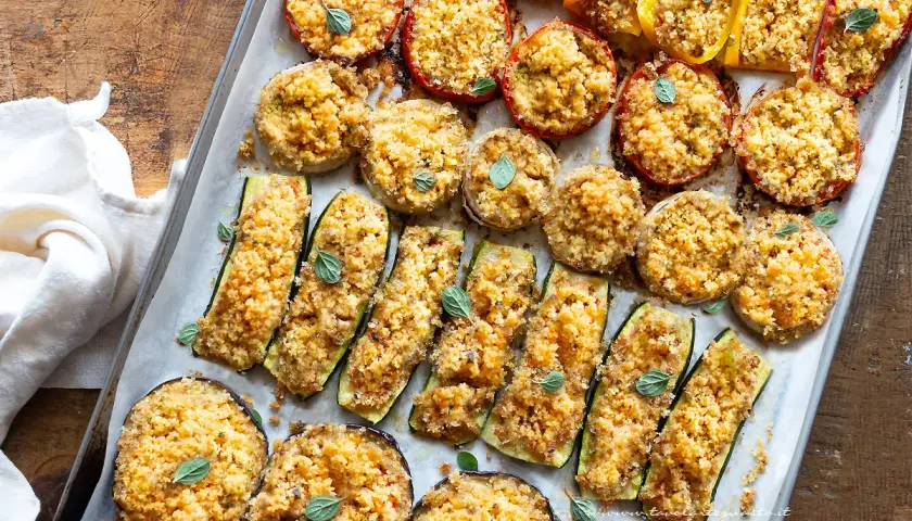 Verdure gratinate al forno: zucchine, melanzane, pomodori e peperoni ripieni di pangrattato e erbe aromatiche, cotti su una teglia.