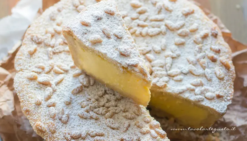 Torta della nonna facile, con crema gialla, pinoli e zucchero a velo. Una fetta è stata tagliata.