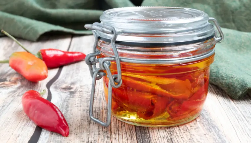 Barattolo di **olio al peperoncino** fatto in casa, con peperoncini rossi freschi accanto su un tavolo di legno.