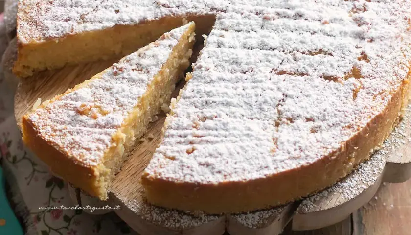 Una fetta di torta di riso, cosparsa di zucchero a velo, attende di essere gustata su un tagliere di legno.