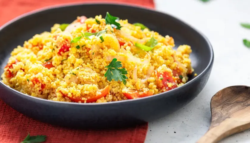 Un piatto invitante di cous cous freddo con pomodorini, cipolle e prezzemolo fresco. Perfetto per un pasto leggero e saporito.