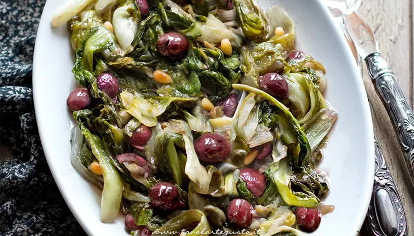 Scarola in padella con olive e pinoli, un contorno saporito e colorato, pronto per essere gustato.