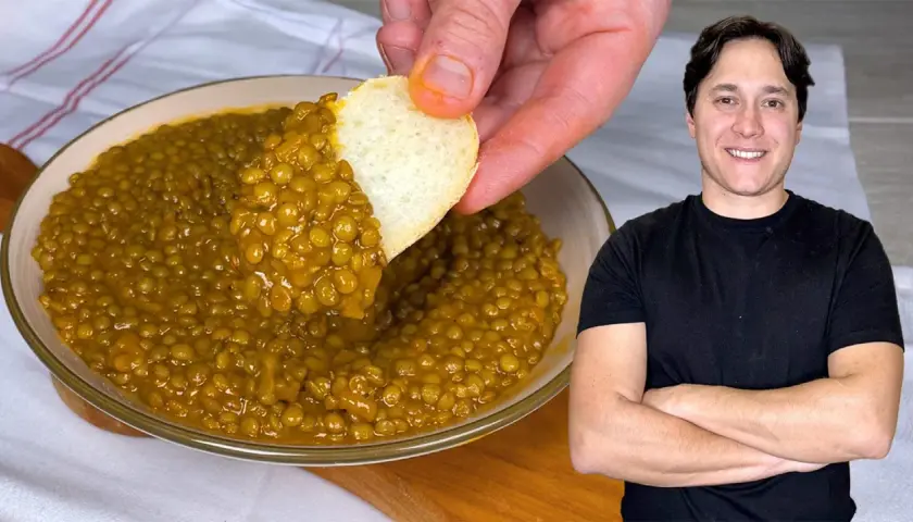 Un uomo sorride mentre un pezzo di pane intinge un piatto di saporite lenticchie in umido.