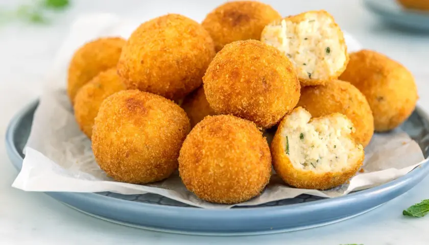 Un piatto di polpette di ricotta dorate e croccanti, alcune intere, altre spezzate per mostrare il ripieno morbido e profumato.
