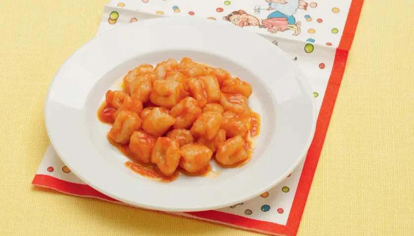 Un piatto di chicche di patate condite con un sugo rosso, servite su un tovagliolo colorato.